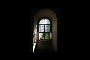 A beautiful architectural window is visible at the end of a dark hallway, with sunlight streaming in.