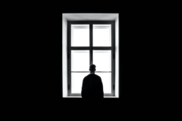 silhouette of a man standing in front of a bright window in a dark room