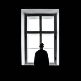 silhouette of a man standing in front of a bright window in a dark room